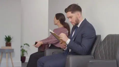 Male And Female Candidates In Office Waiting For Job Interview Looking At Mobile Phone And Reading Notes 3