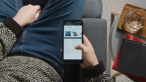 Overhead Shot Of Person At Home Shopping Online Looking At John Lewis Website On Mobile Phone On Black Friday