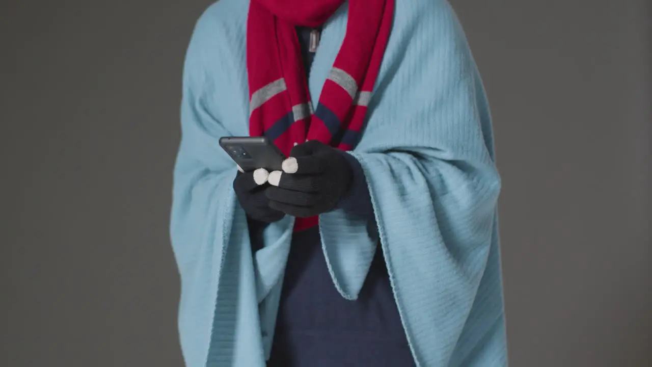 Close Up Of Person Wearing Blanket And Gloves Using Mobile Phone Trying To Keep Warm In Energy Crisis