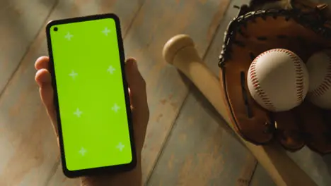 Person Holding Green Screen Mobile Phone Above Baseball Still Life With Bat Ball And Catchers Mitt On Aged Wooden Floor 1