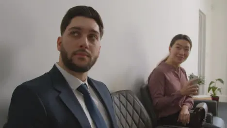 Male And Female Candidates In Office Waiting For Job Interview Looking At Mobile Phone And Reading Notes