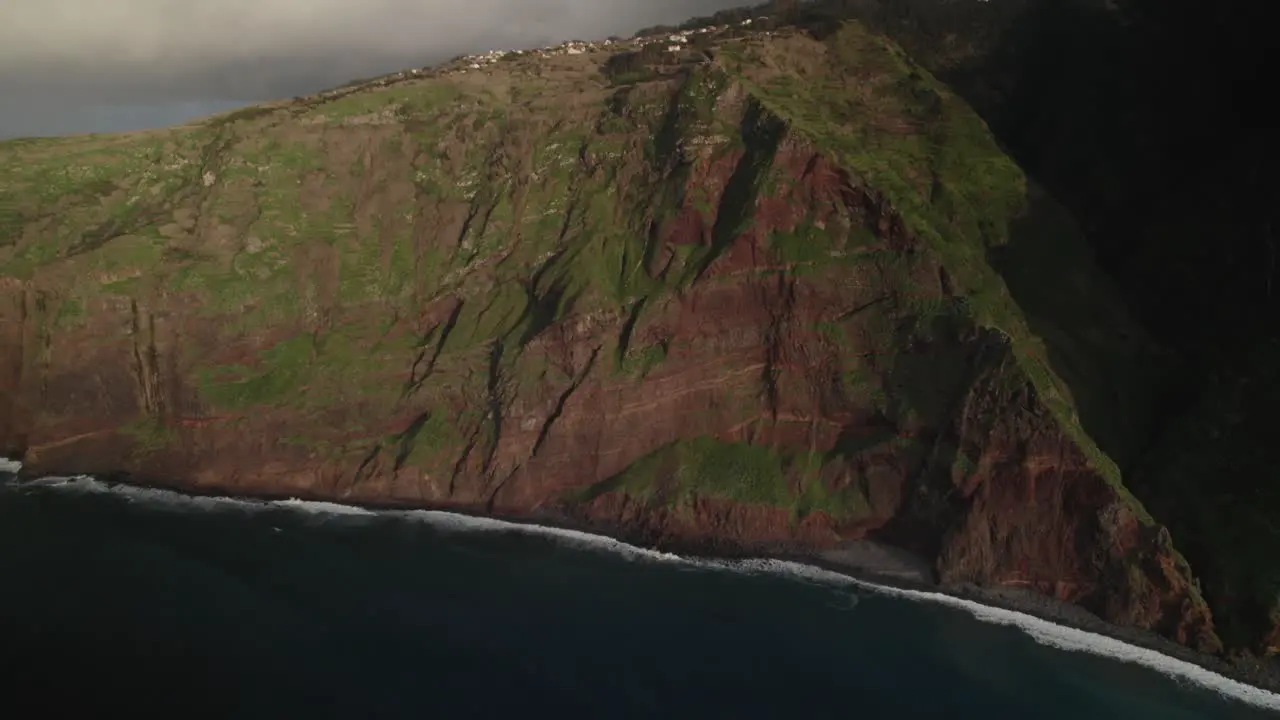 Aerial view with drone of a rugged cliff coastline with lush greenery mountain and ocean waves in cloudy weather in Madeira