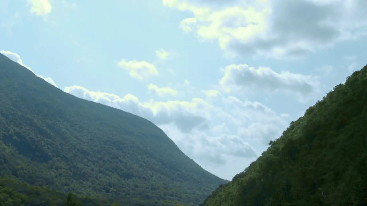 Green mountains stand beyond a calm lake as the camera tilts from a cloudy blue sky