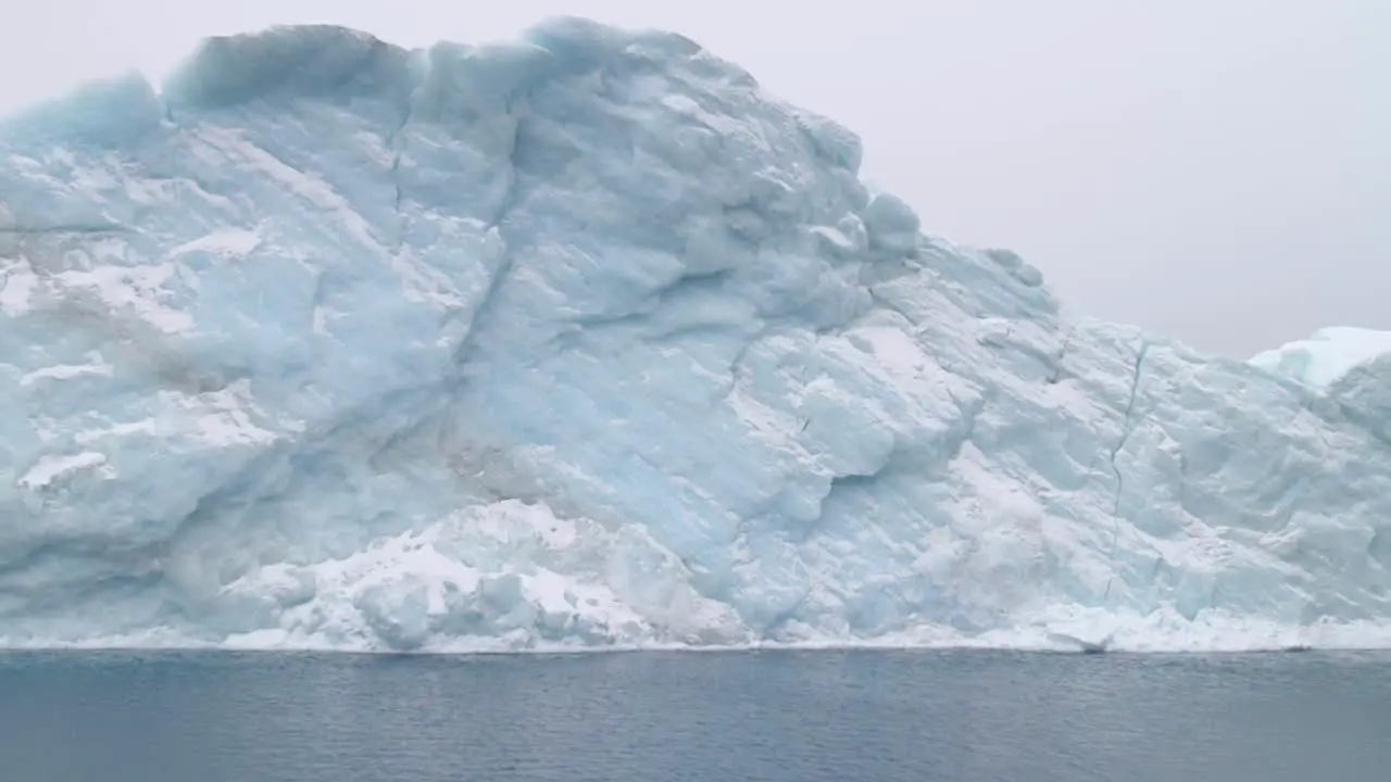 Aquamarine blue iceberg floats on the ocean on a cloudy day