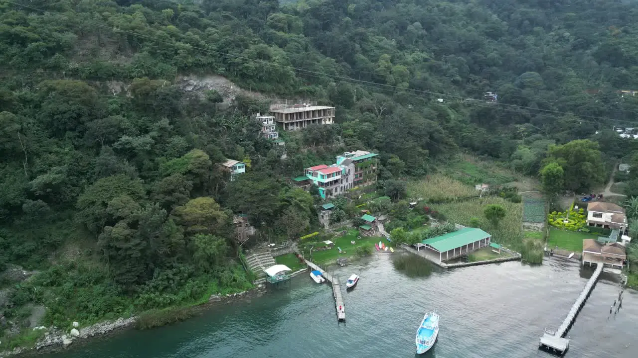 Drone view in Guatemala showing a hotel on a green hill facing a blue lake on a cloudy day in Atitlan