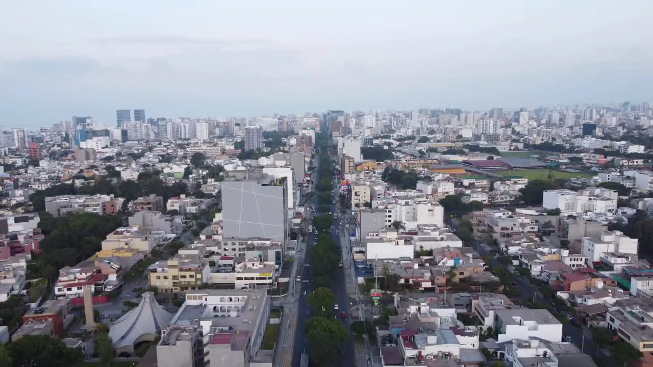 Drone flying forward above a street called "Avenida Benavides" with many trees in the middle of the 2 lanes going into the distant horizon of the city