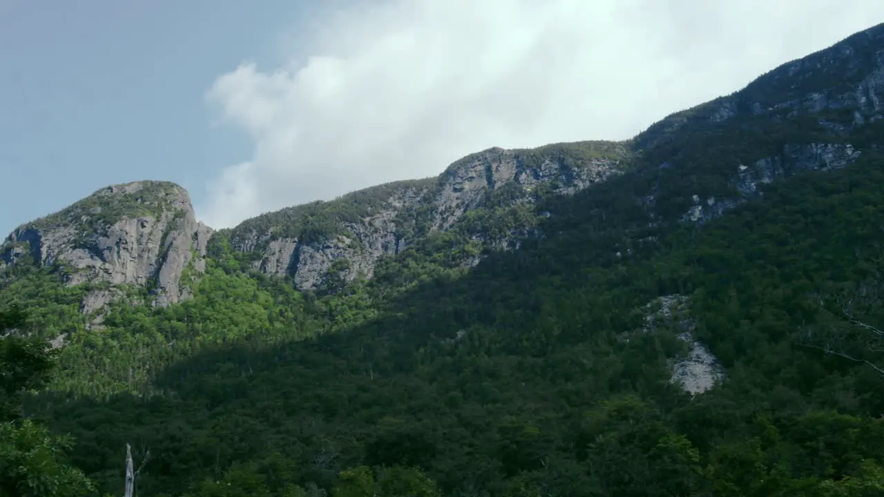 Granite mountains stand against a blue sky filmed at a low angle to emphasize their size as the camera pans to a road through the mountains