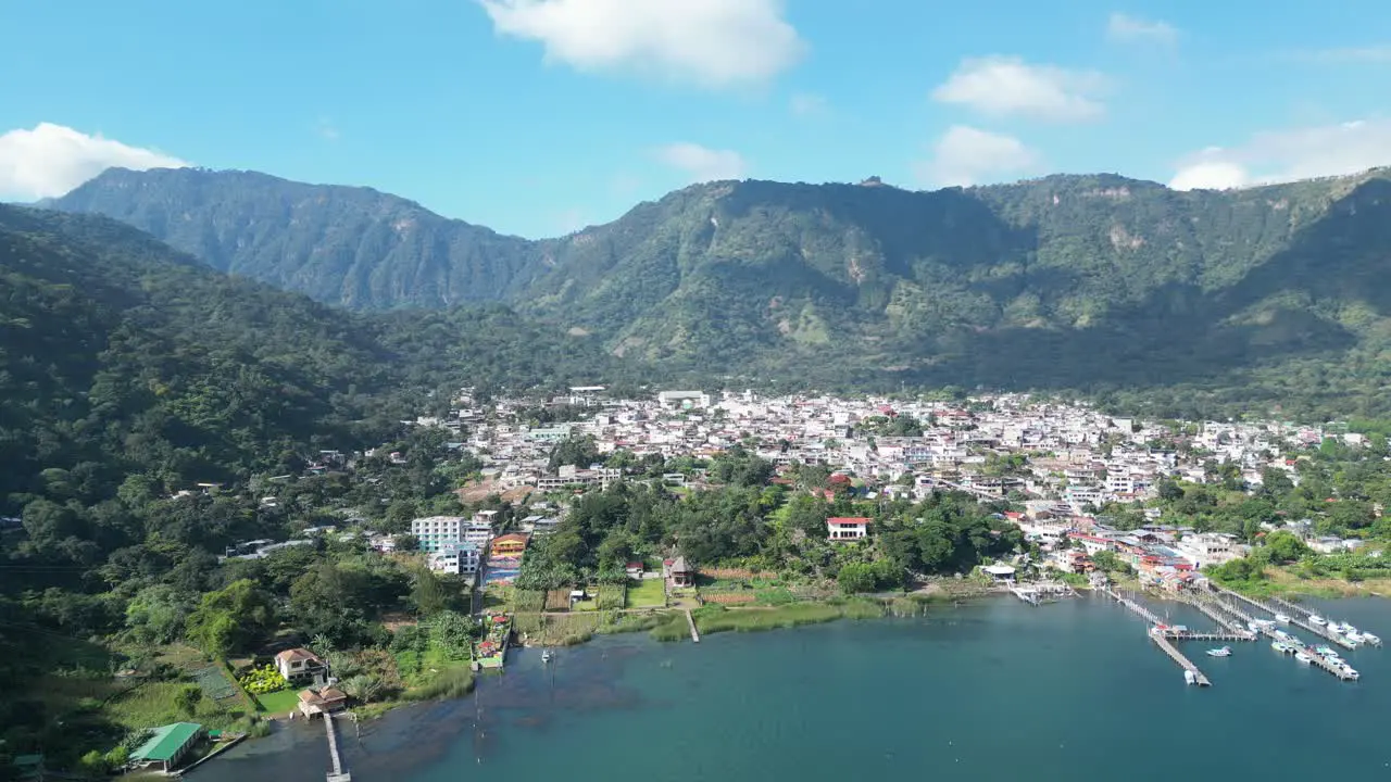 Drone view in Guatemala flying over a blue lake surrounded by green mountains and volcanos and a town on a sunny day in Atitlan