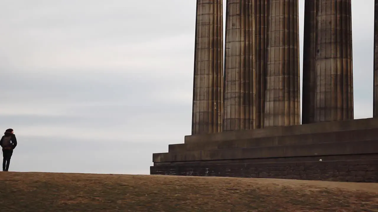 Traveler walking next to giant pillars Edinburgh Scotland cloudy static shot