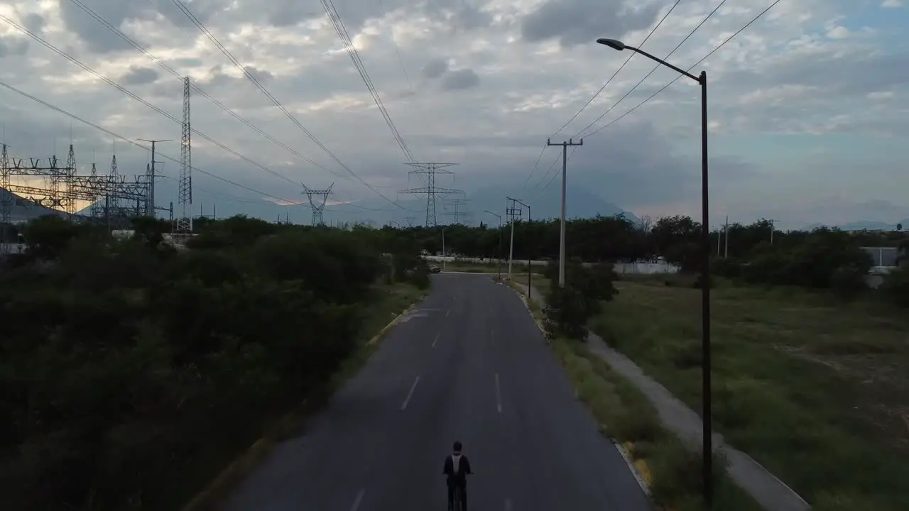 guy going in the middle of electric towers in his bike in a lonely street in a beautifull day