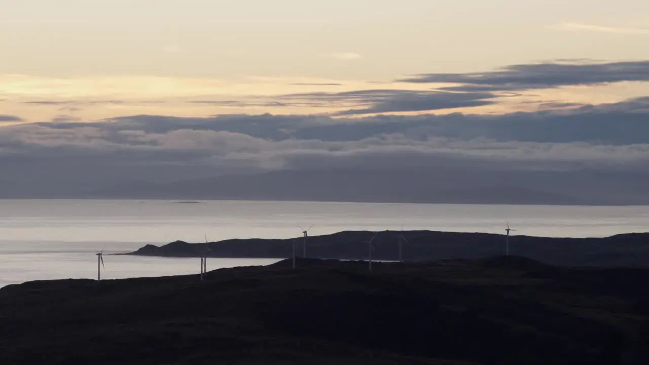 Beautiful New Zealand landscape with ocean and distant mountain during sunset with windmills