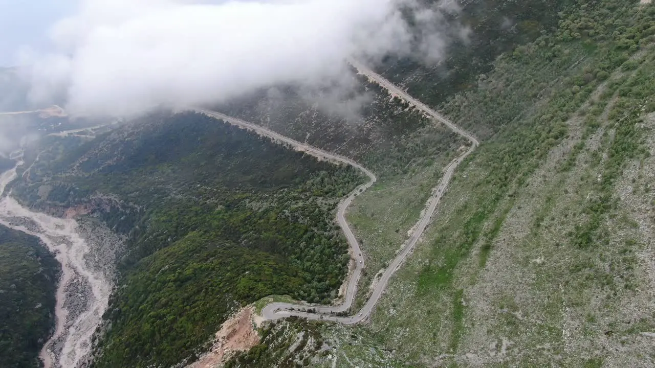 Drone view in Albania flying over a green and rocky mountain with serpent road climbing a port on a cloudy day