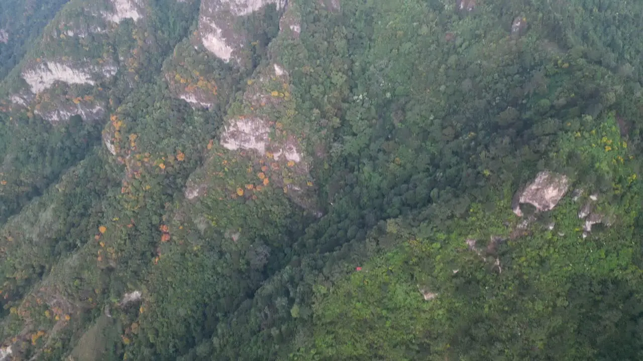 Drone view in Guatemala flying over green forest on a mountain top view and panning up to show a three peak mountain on a cloudy day in Atitlan