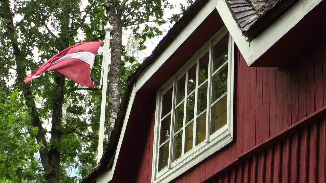 Latvian Flag Waving Next to a Old Red House