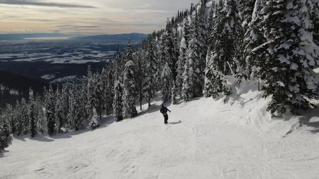 Ariel Drone following a snowboarder through the mountains doing slower movements showing off a beautiful late sunrise