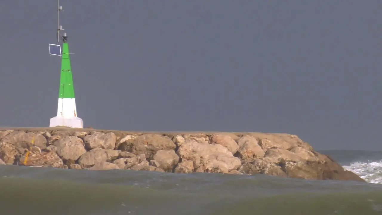 Wave breaking over sea wall with harbor light slow motion