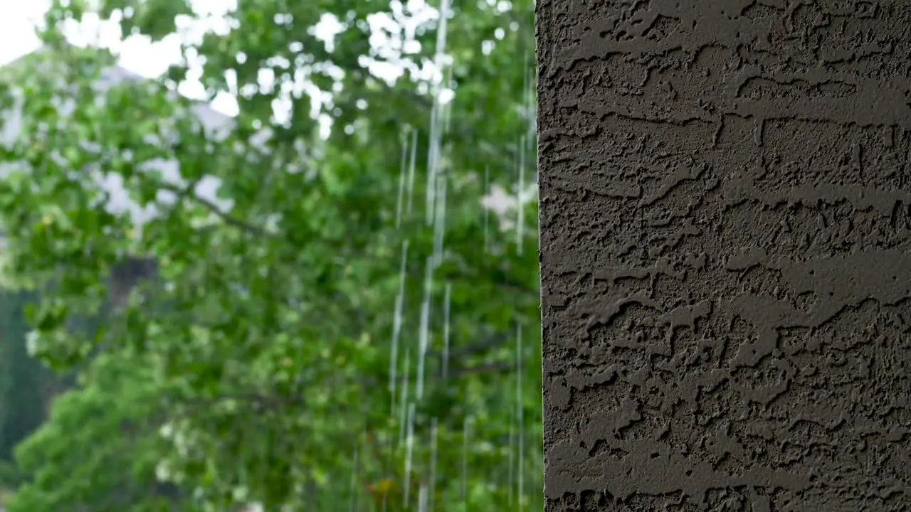 Rain pouring down gutters along a concrete balcony wall with trees in background