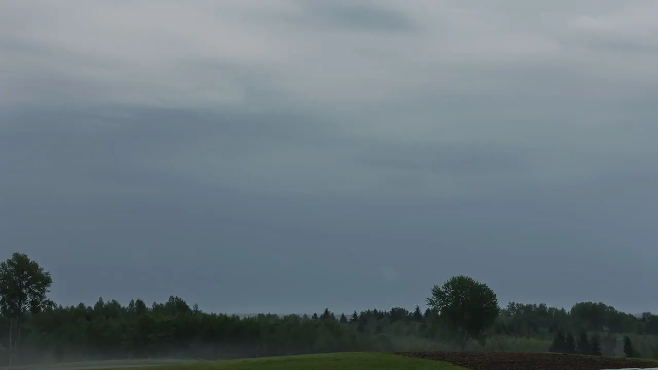 Timelapse of dark clouds above a forest and a field