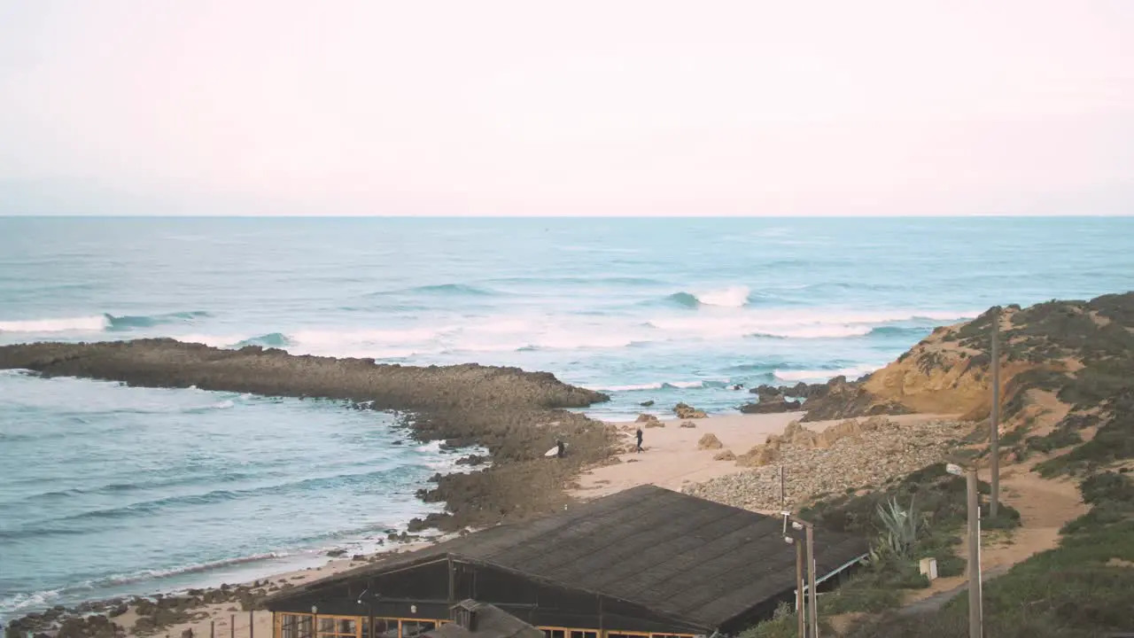 Surfers walk over rocks to reach surf