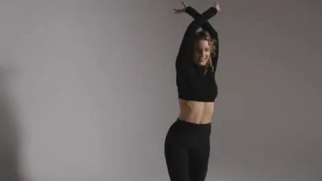 Three Quarter Length Studio Shot Of Young Woman Doing Dance Practise Against Grey Background