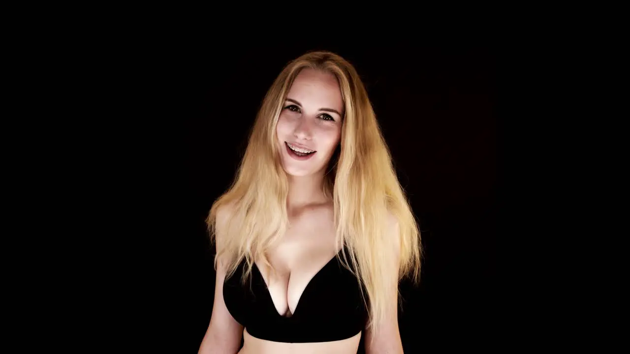 Beautiful young woman with big natural breasts in a black bra on a black background laughing at the camera