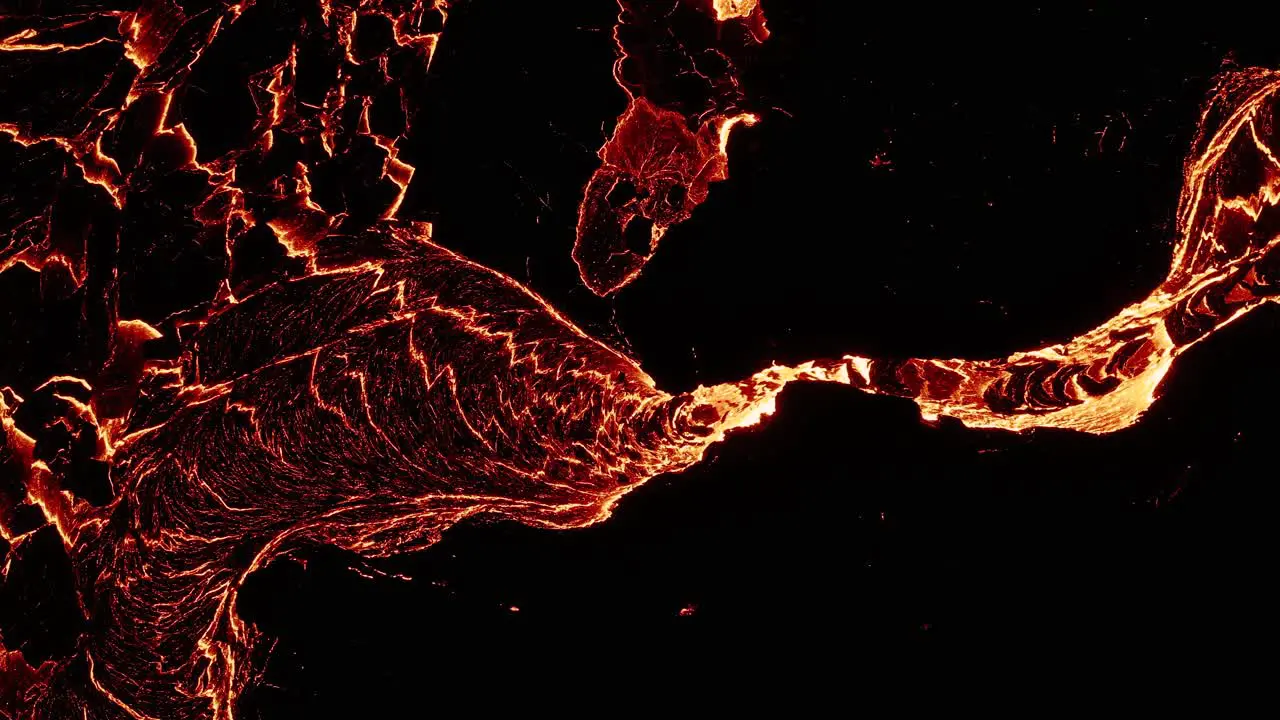 Molten lava flows through dark rock surface solidifying and cracked top down