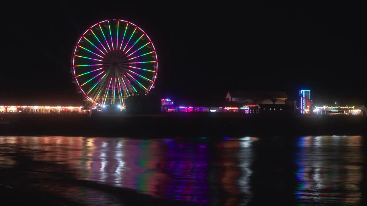 Big Wheel ride and amusements at night with lights reflecting from the incoming tide at Central Pier Blackpool Lancashire England UK