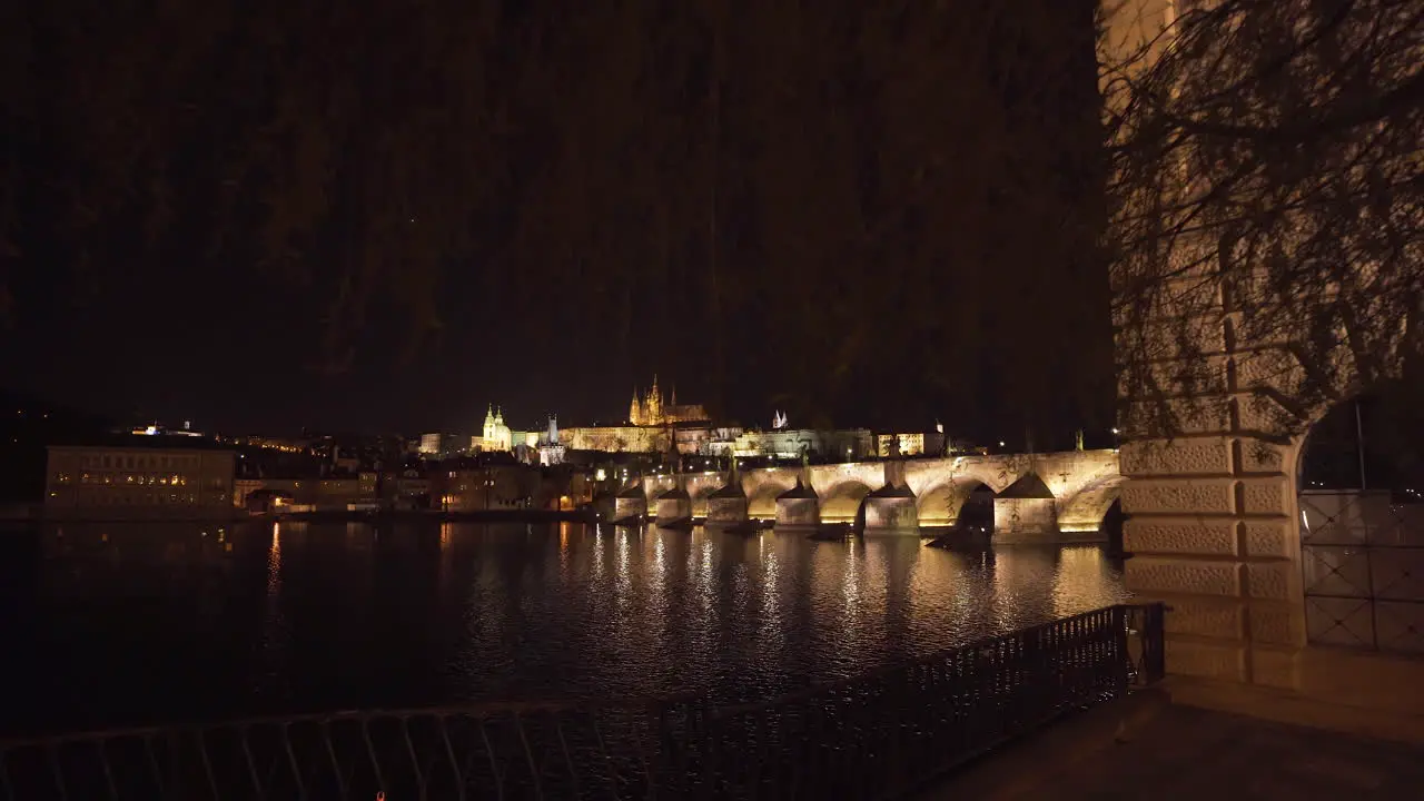 The Prague Castle and Charles bridge over river Vltava in the historical centre of Prague Czechia lit by lights at night shot from the other side of the river zooming through willow branches