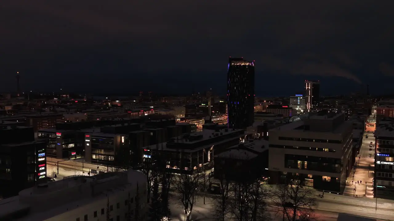 Aerial view low over night lit streets and buildings towards the Torni hotel and the railway station winter in Tampere city Finland