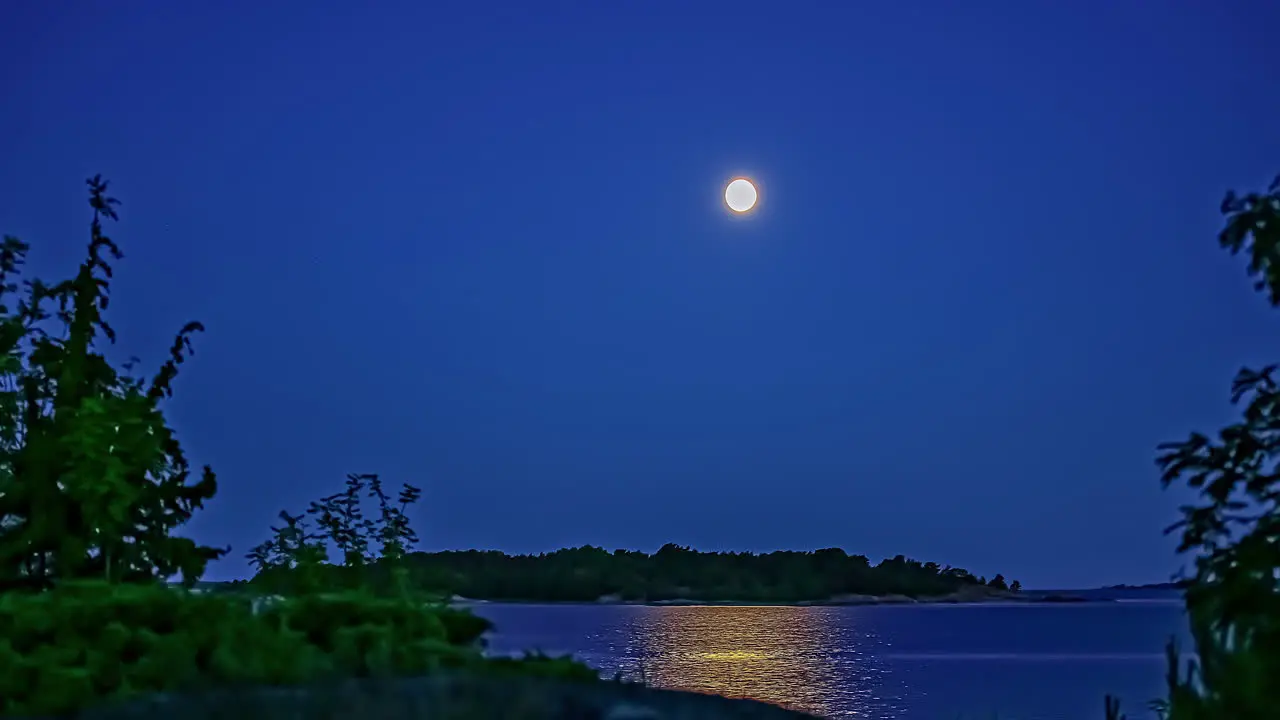 Full moon crossing the sky over an island across a bay nighttime time lapse