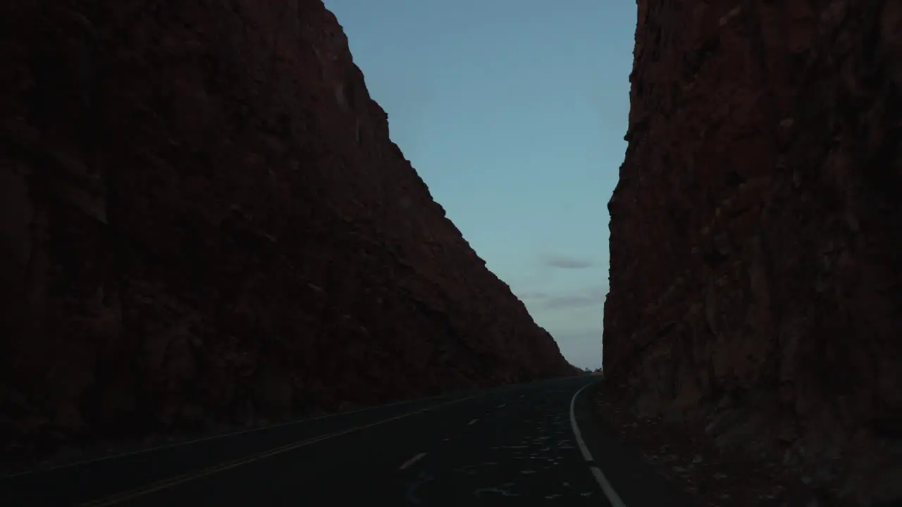 Driving down a desert road in between tall rock walls at dusk Concept dark road eerie alone discovery exploration roadtrip camping