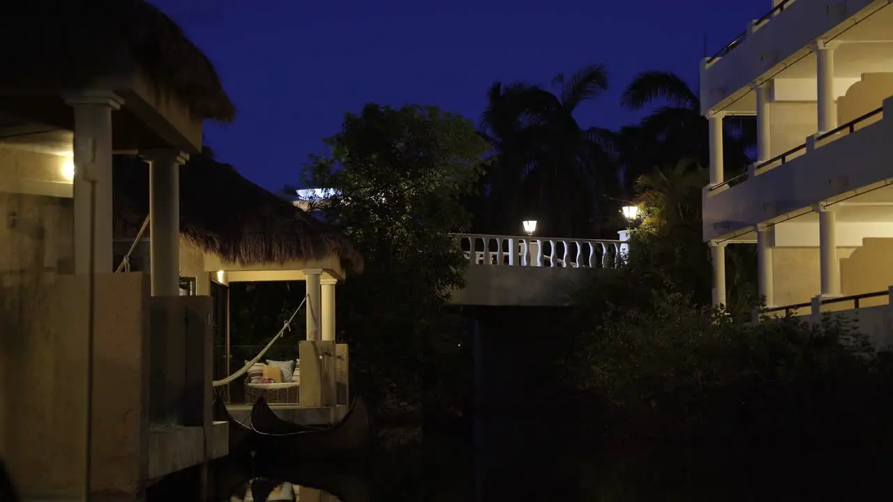 Tranquil night time scene of small tropical bungalow's along a small river with a car driving by on the illuminated bridge above in a vacation resort in Riviera Maya Mexico near Cancun and Tulum