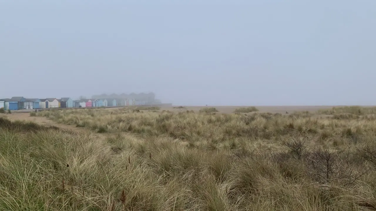 Beach huts on a misty winter coastline and grassy sand dunes beneath a foggy grey sky