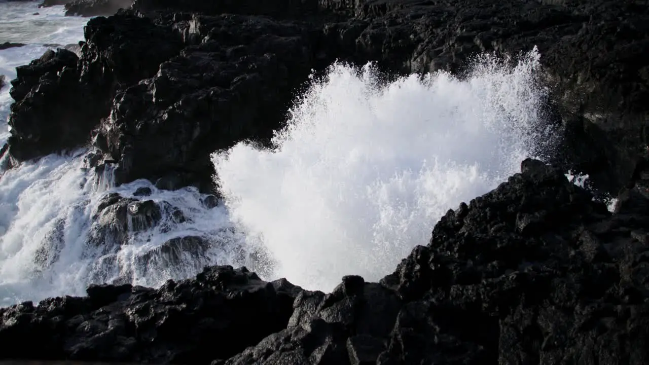 Wave crashing on dark black basalt rock shore of volcanic island