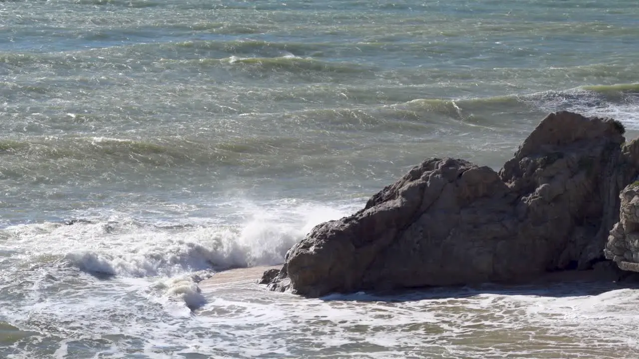 Rough sea with waves hitting the rocks on the beach at midday