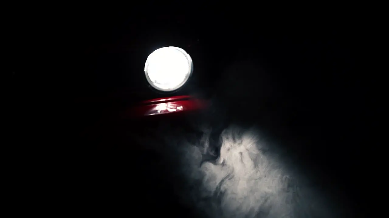 Fog or mist moving in light beam of red car round headlight slow motion close up