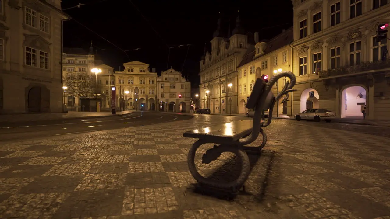 A bench on the empty Malostranské square with a tram stop and rails in the historical centre of Prague Czechia at night lit by street lights during a Covid-19 lockdown with no people anywhere