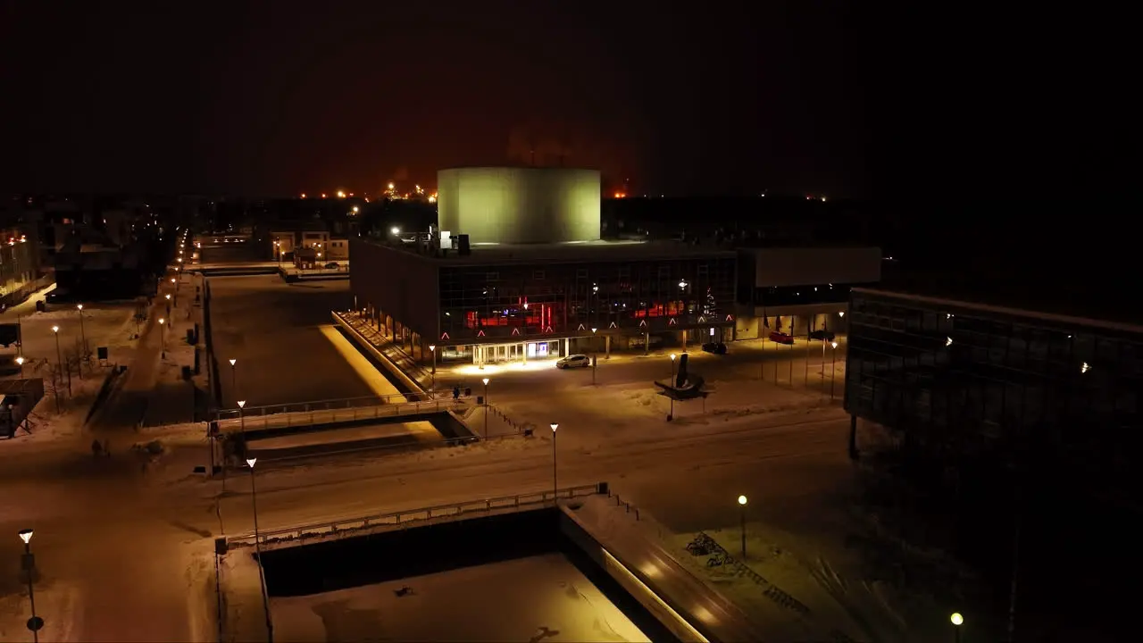 Aerial view ascending in front of the illuminated Oulu Theatre winter night in Finland