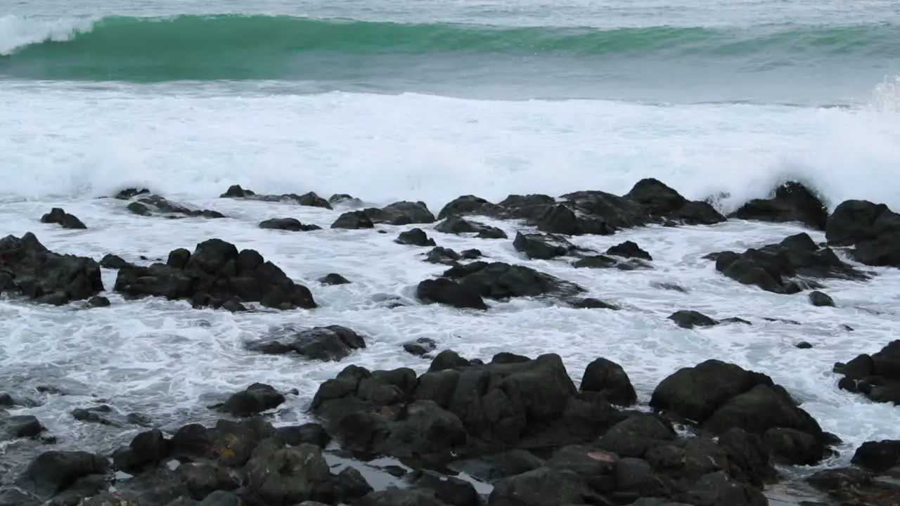 Close-up view of rocks offshore crashed by strong sea waves and reflecting on and across stones during the day in slow motion capture at 120fps