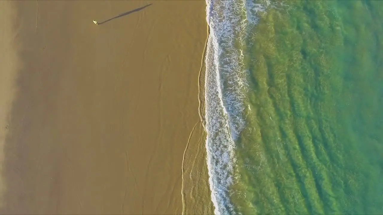 Aerial shot looking directly down and offering a bird's eye view of the crystal clear aquamarine waters off the beach of Fraser Island and over the sands and tire tracks from 4x4 trucks