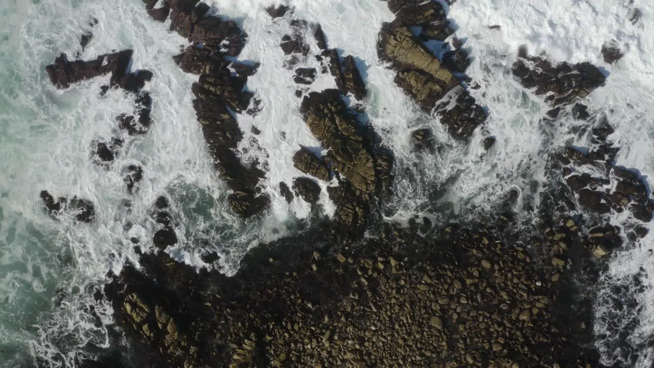 4K overhead corkscrew of stormy seas breaking on rocks as a seagull crosses the frame