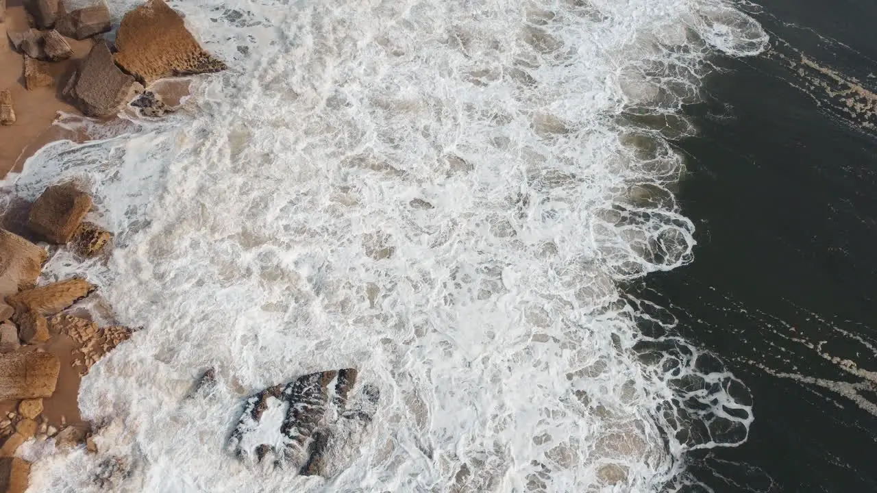 Aerial view of waves breaking at rocky shoreline in Nazare Portugal