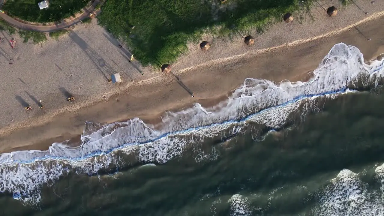 Aerial birds eye descending over beach with unrecognizable people walking