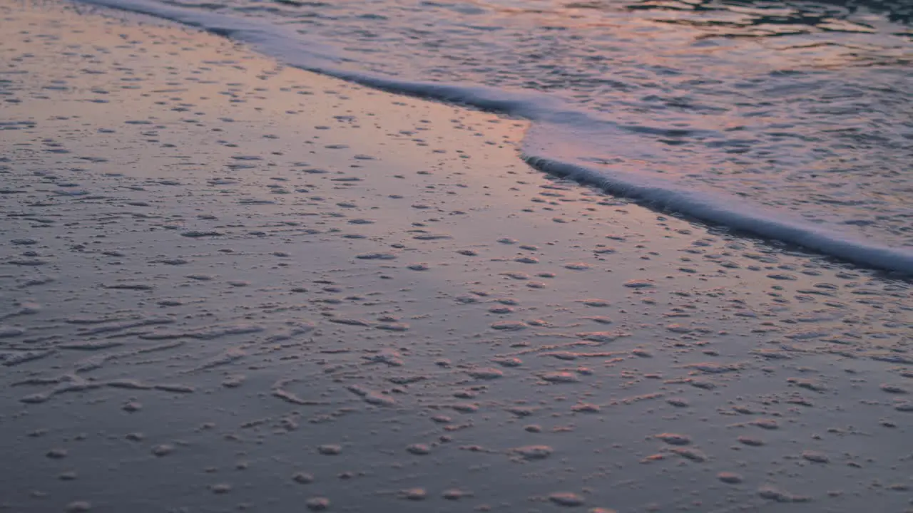 Calm sea waves reaching the sandy beach creating texture with white sea foam