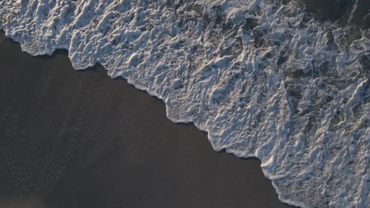 Majestic ocean waves rolling over sandy beach leaving foamy trace aerial top down shot