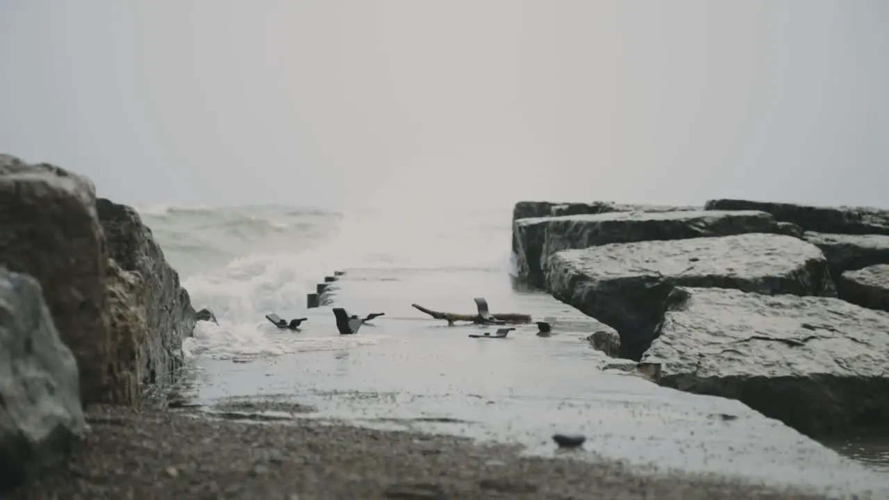 Waves Crashing Over Breakwater Rocks And Seawall At Beach During Stormy Day