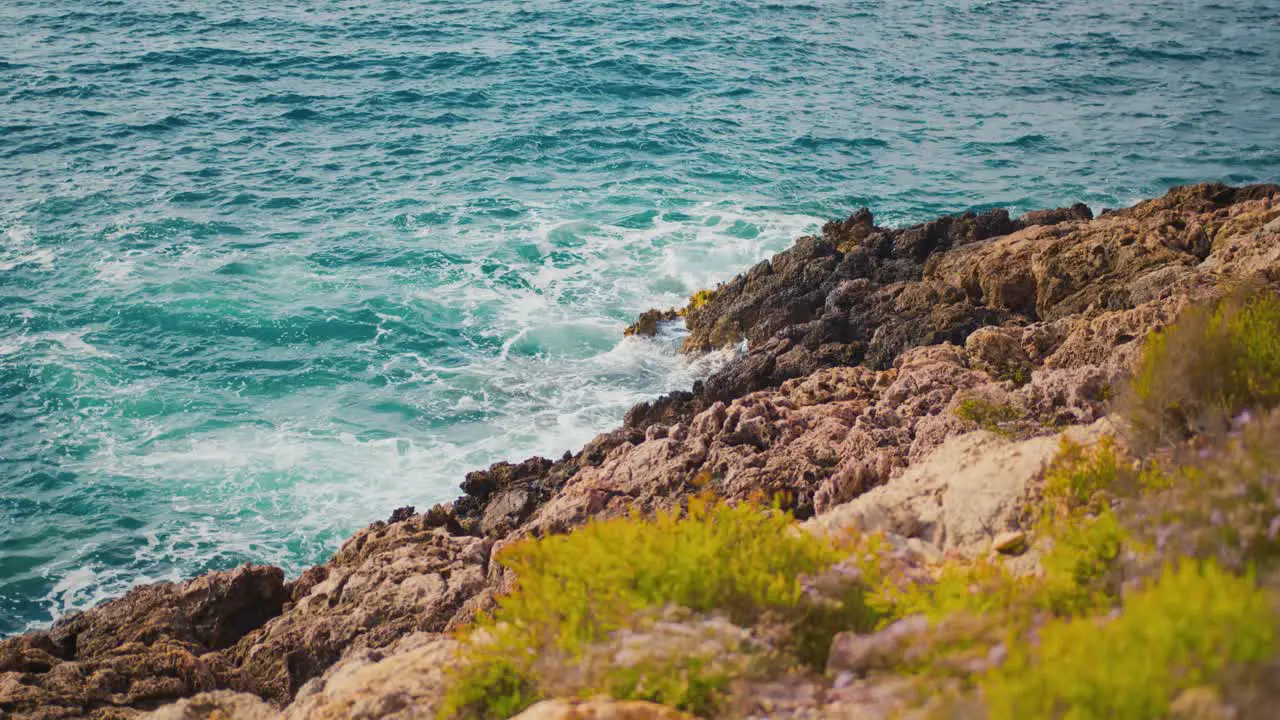 The ocean waves crash against the mountain rocks on a sunny day