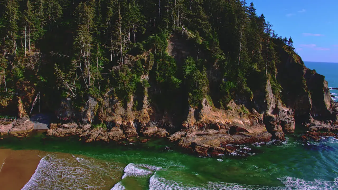 Aerial flying forward rising over beach waves revealing ocean cliffs trees