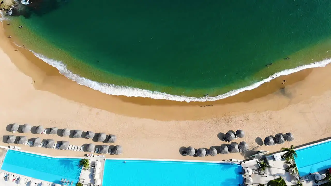 beach waves and ocean topview in slowmotion Huatulco Mexico aerial drone descending zoom in to beach resort with swimming pool