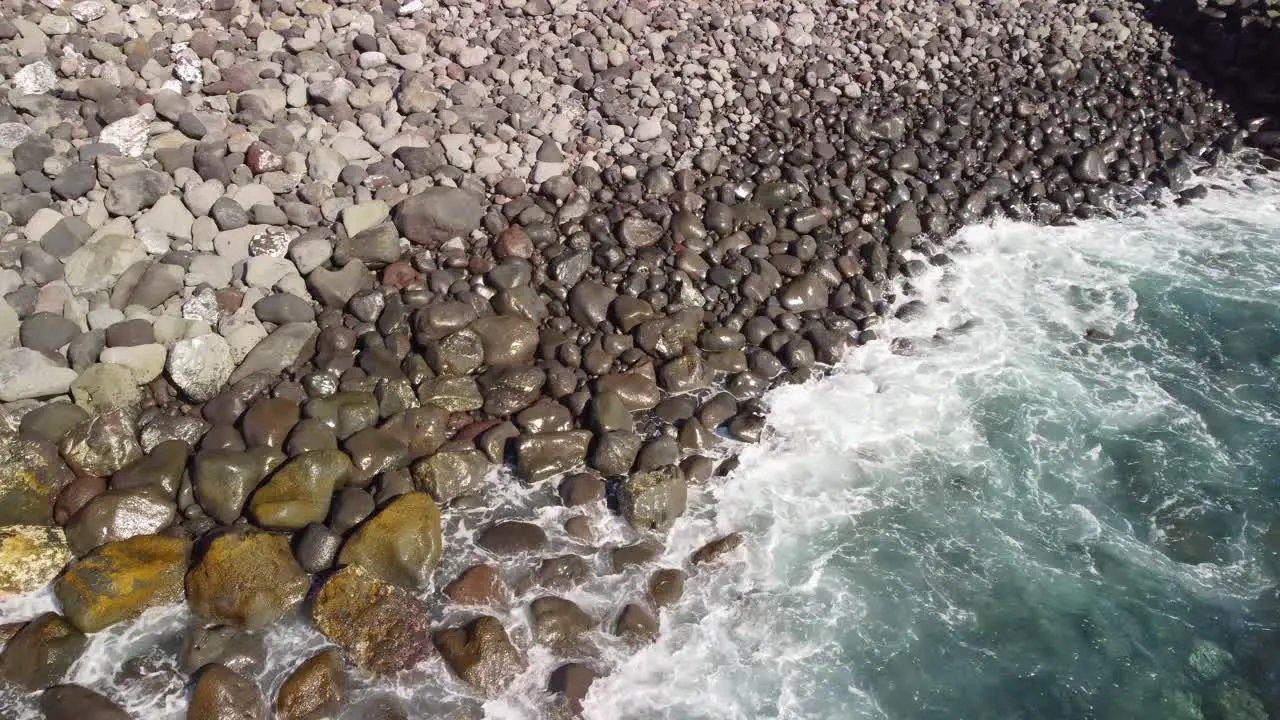 Aerial slow view at blue waves crashing into beach made from small stones